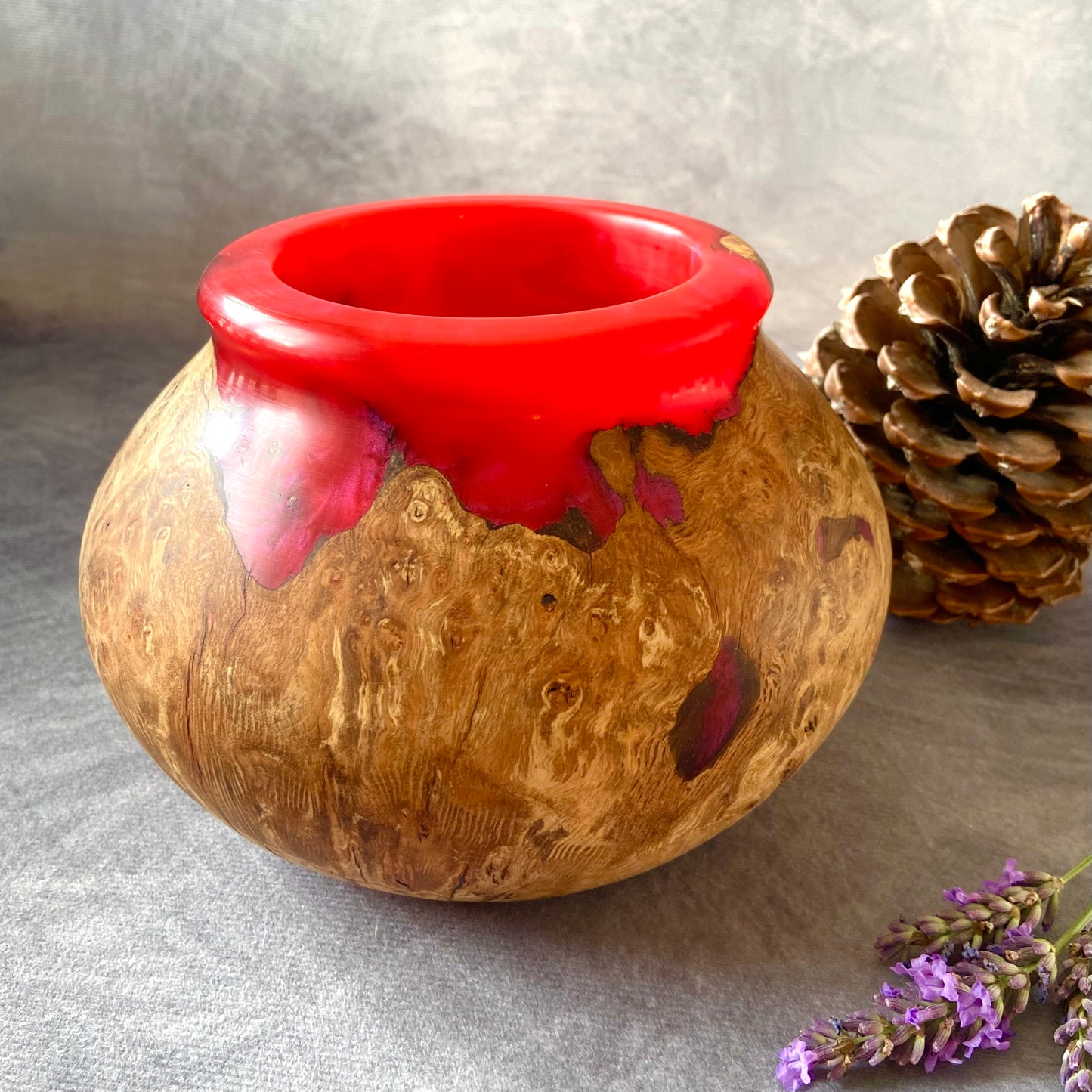 Vase with red top and wooden base on a gray surface with a pine cone and lavender.