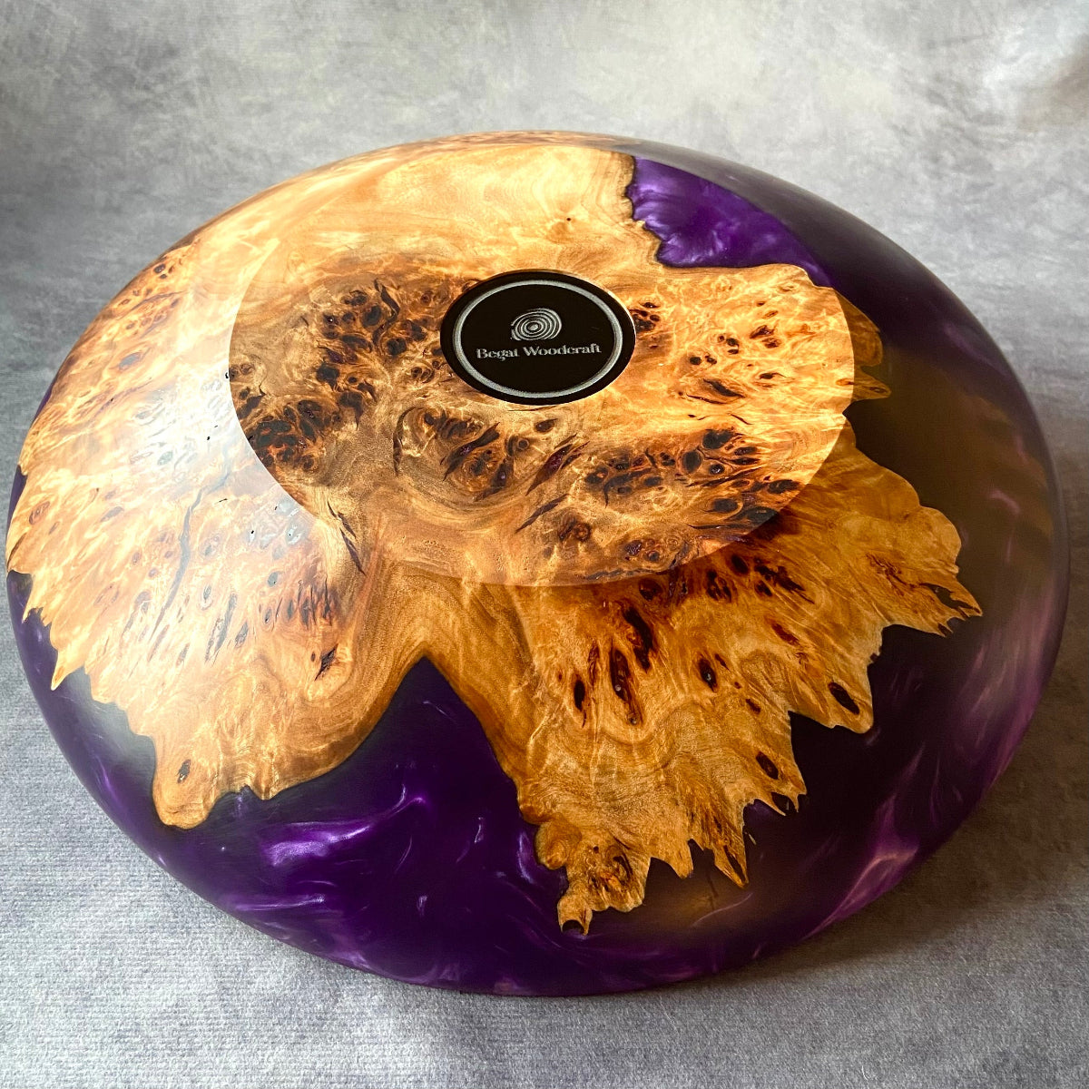Base of handmade mappa burr and purple resin bowl – polished epoxy and burl wood art featuring Begat Woodcraft logo and intricate natural grain.