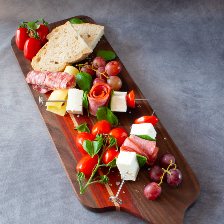 Charcuterie board containing meats cheese grapes tomatoes basil leaves