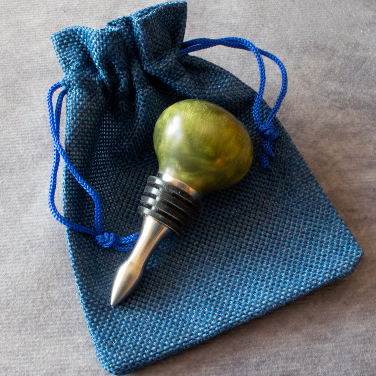 Wine stopper in olive green resin displayed with cloth bag