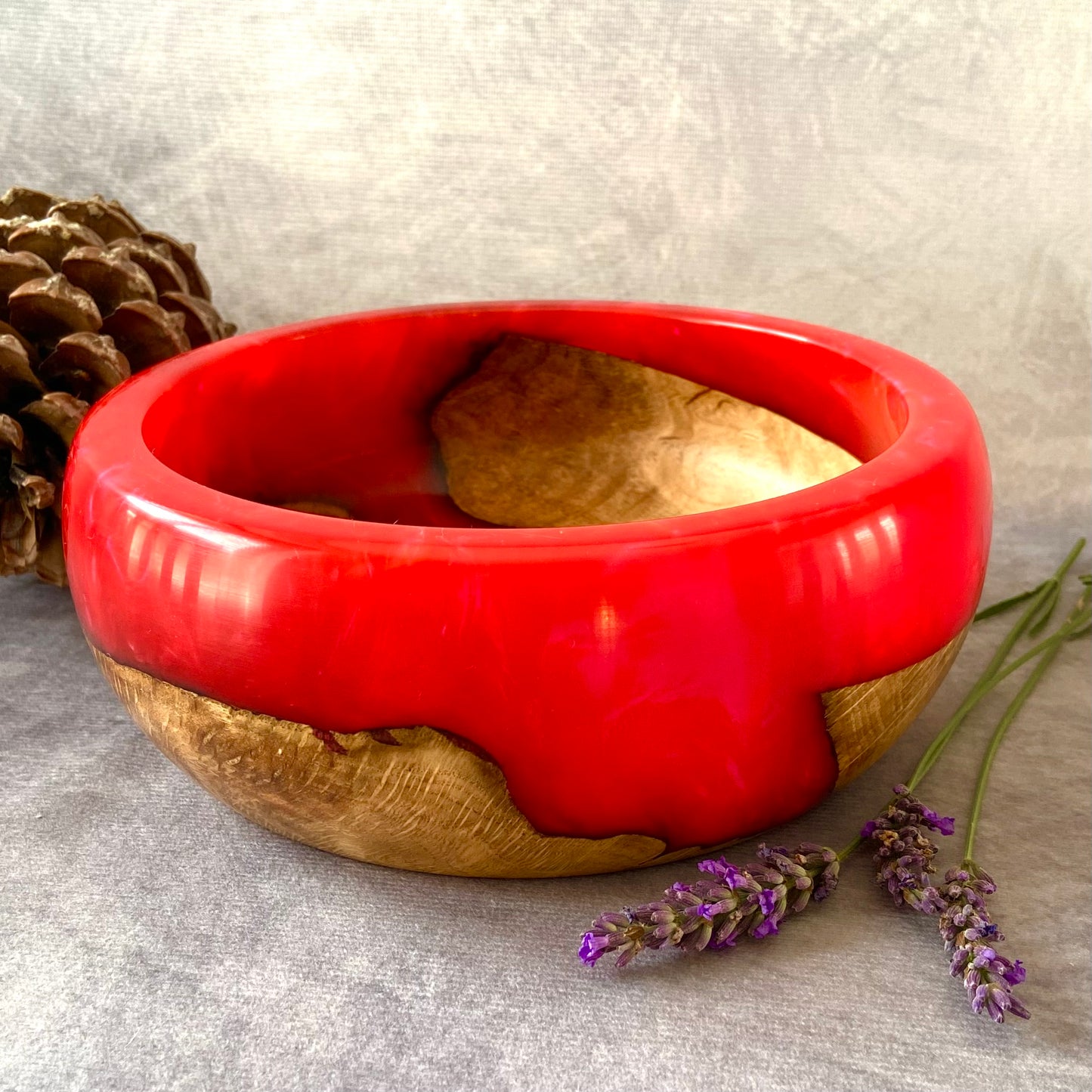 Red and wooden bowl with lavender and a pine cone on a gray surface