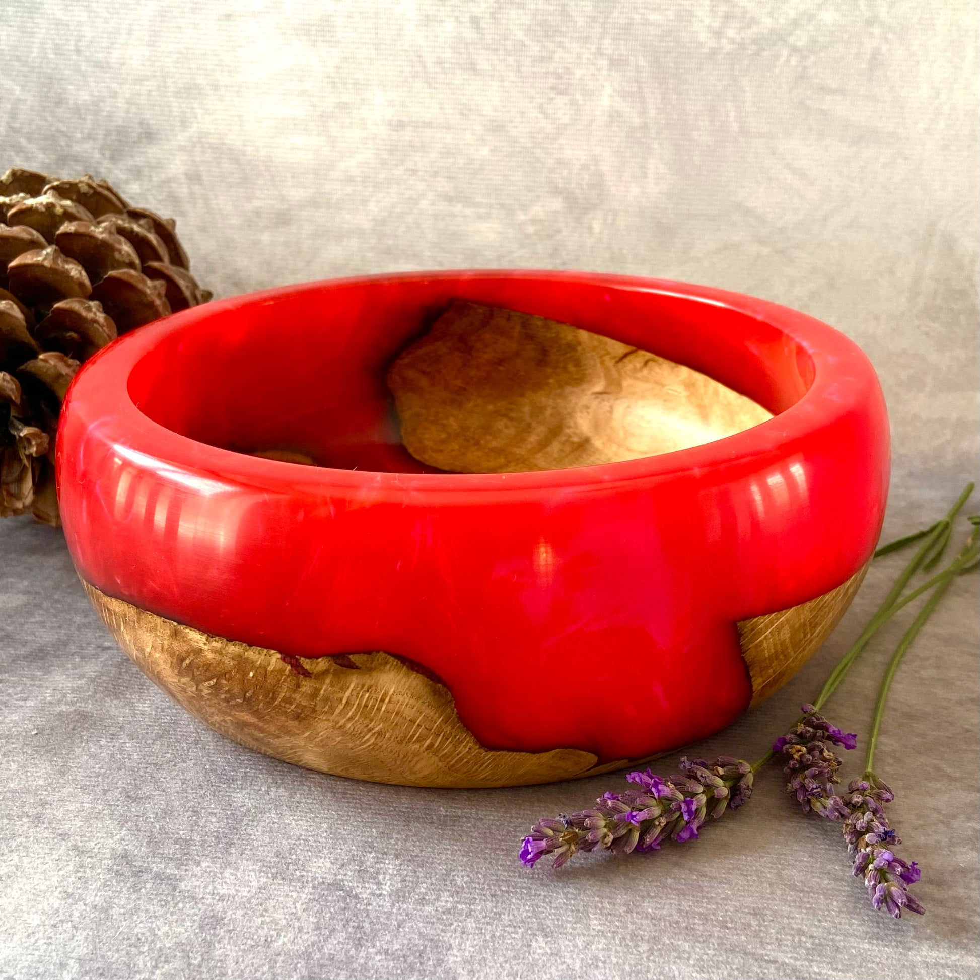 Red and wooden bowl with lavender and a pine cone on a gray surface