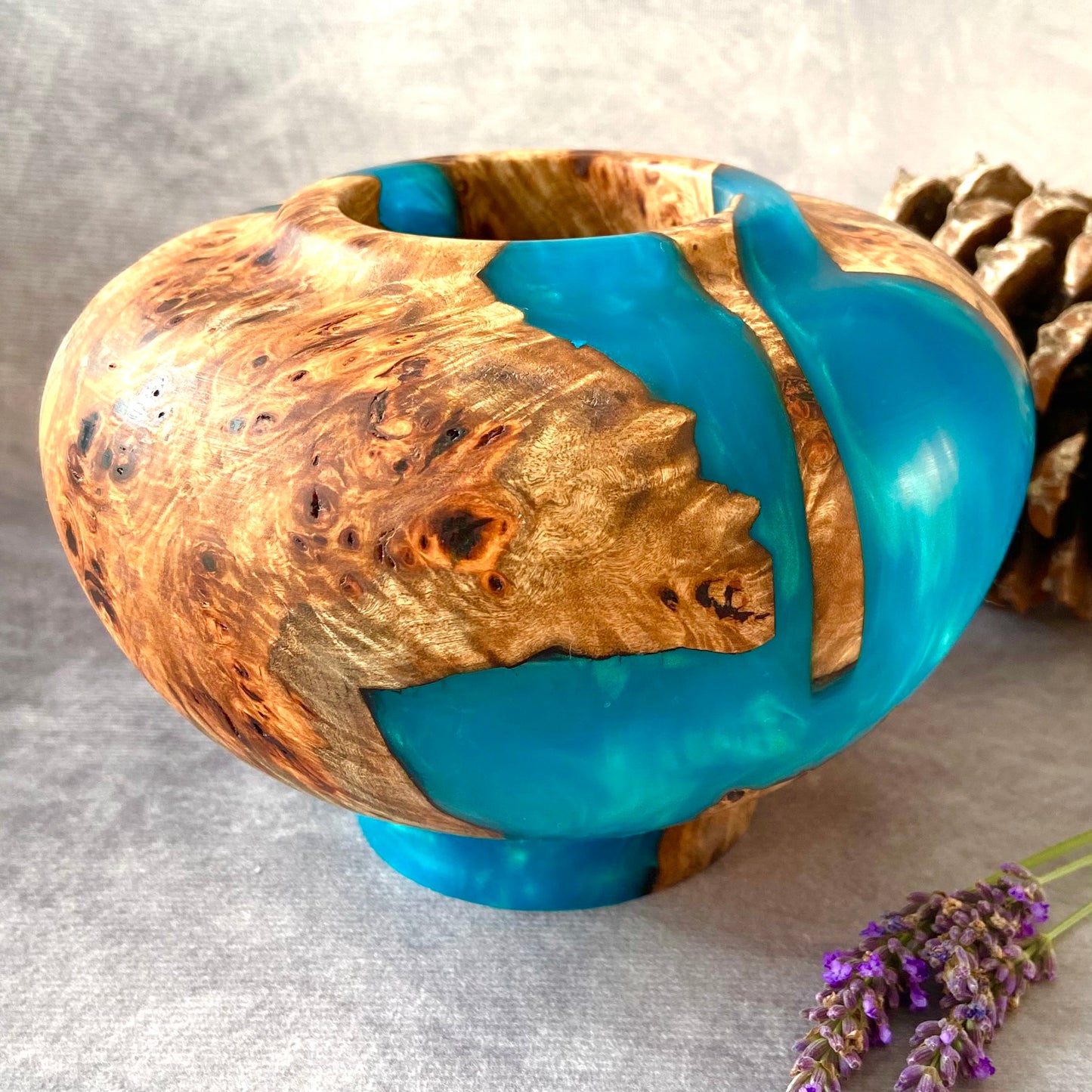 Wooden bowl with blue resin on a gray surface with lavender flowers.