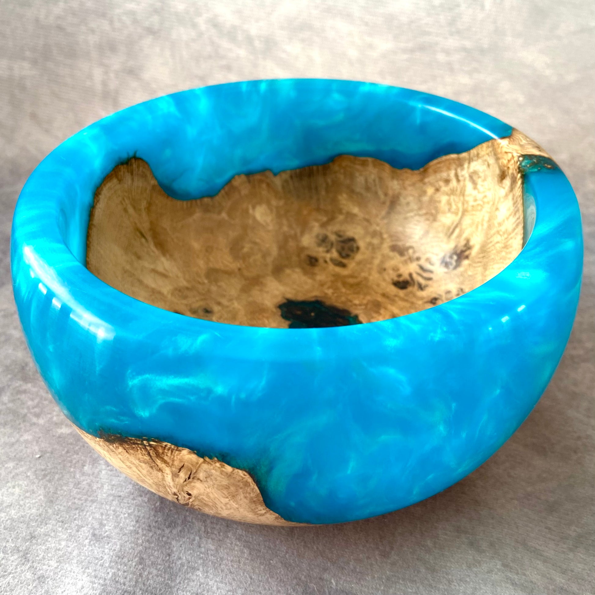 Blue resin bowl with natural wood edge on a gray background