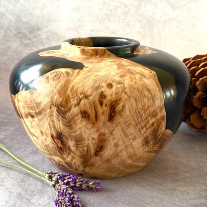 Wooden vase with black top on a gray surface with lavender and a pine cone.