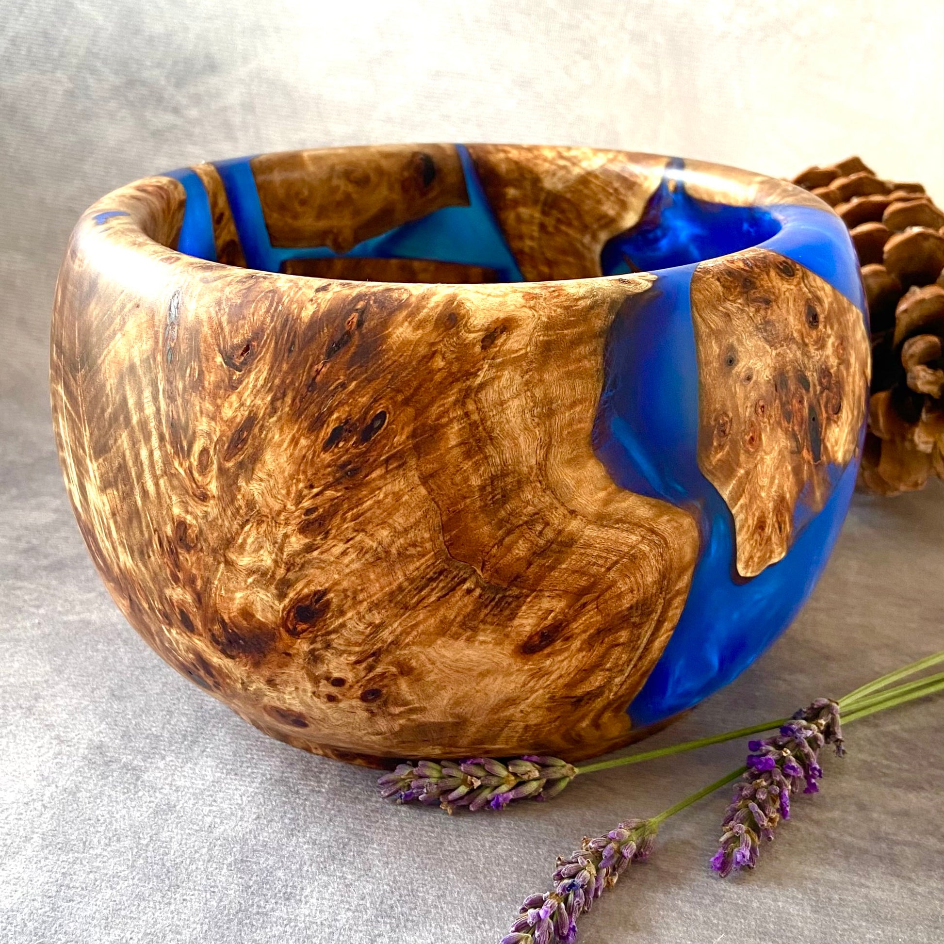 Wooden bowl with blue resin inlay on a gray surface with lavender and a pine cone.