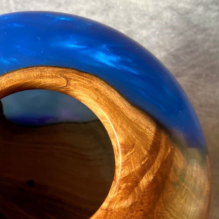 Close up texture of English Apple Wood grain meeting glass-like cobalt resin