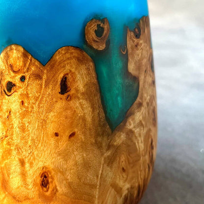 Close up detail of natural pale grain and jewel tone turquoise resin on a turned wood vessel.