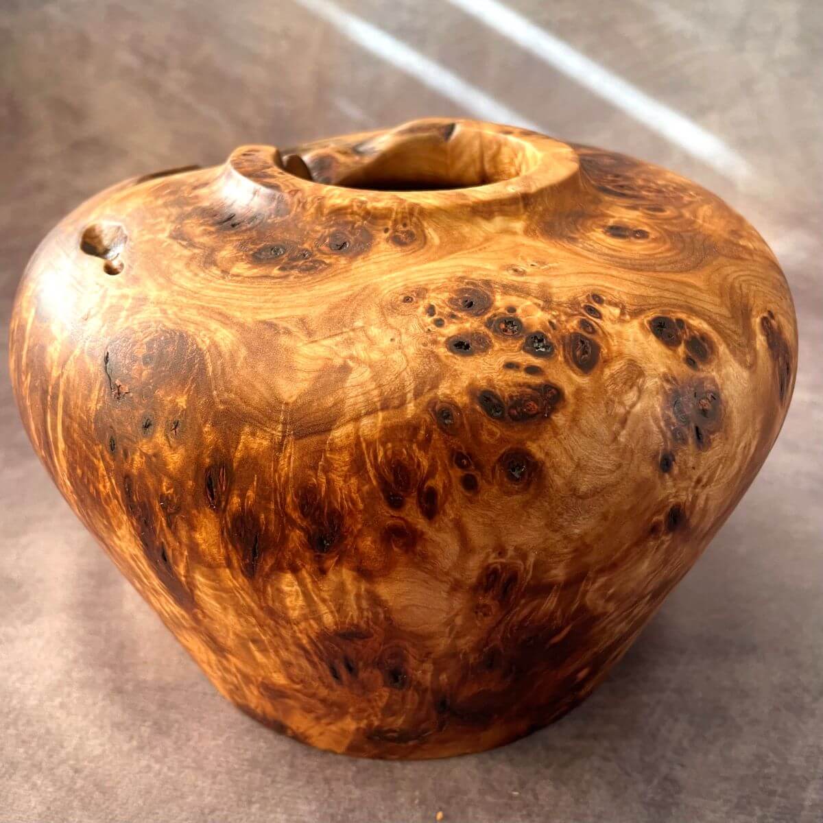Side view of a Mappa burr turned wood vessel with natural live edges and voids.