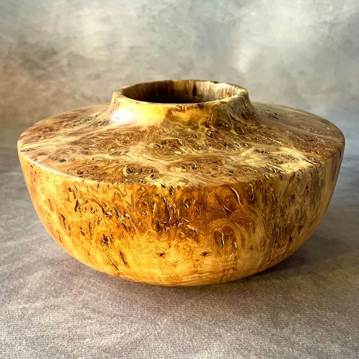 Angled view of a hand turned mappa burr art vessel highlighting its smooth sweeping curves.
