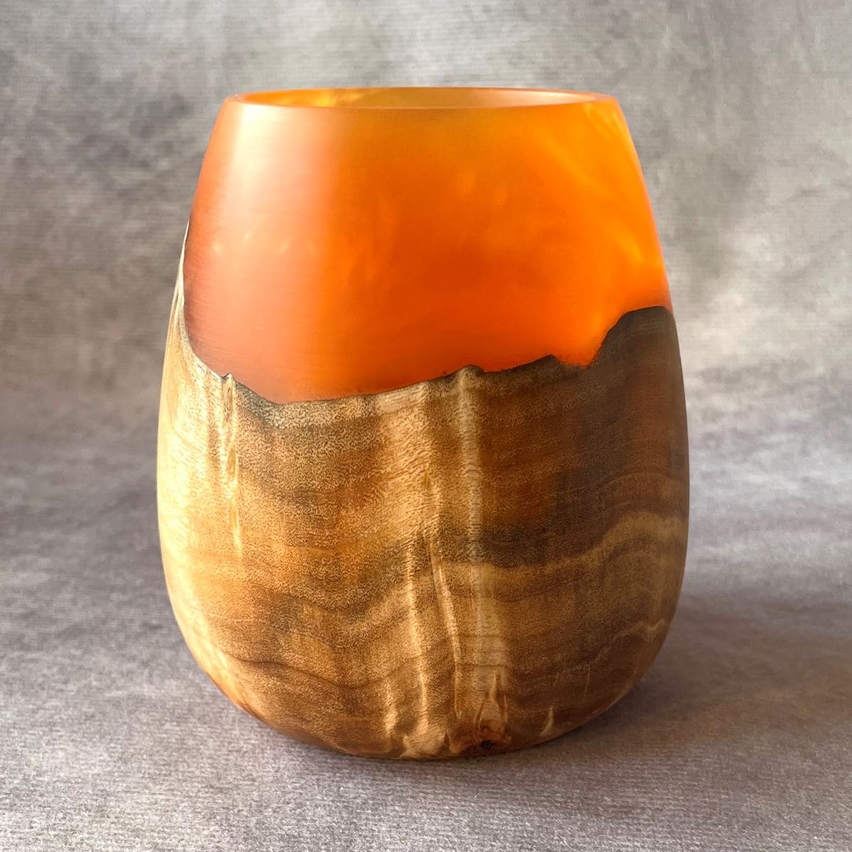 Vase with orange top and wooden base on a gray background