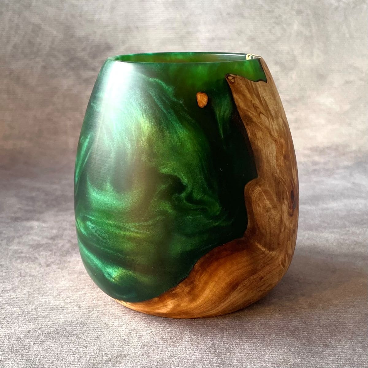 Vase with green marbled design and wooden base on a gray background