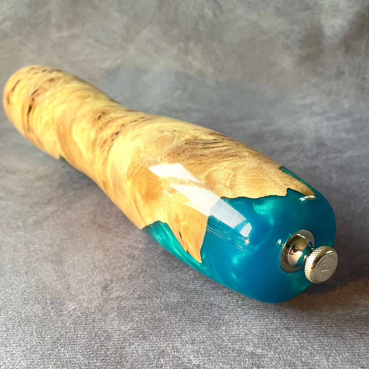 Handmade Mappa Burr and turquoise resin pepper mill displayed on the side