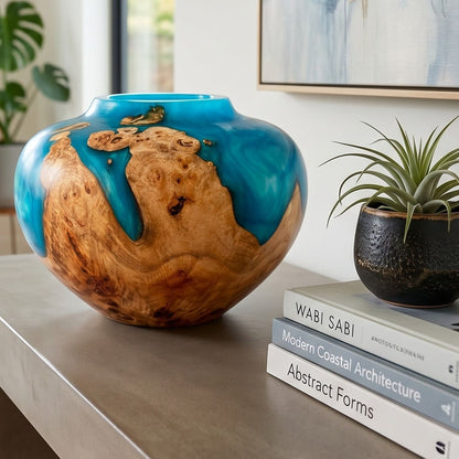 Decorative vase with wooden texture and blue glaze on a surface with books and a plant.